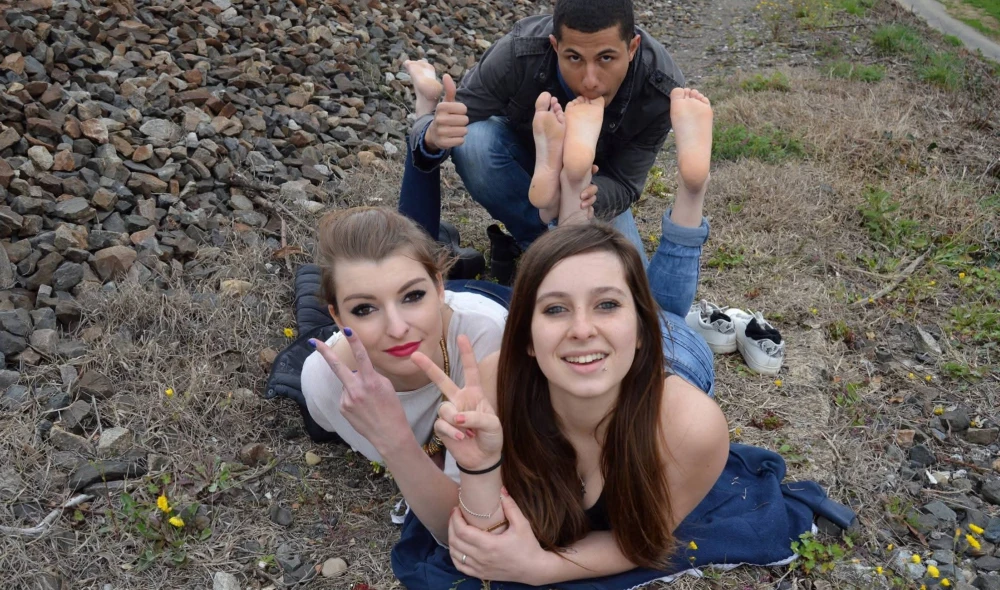 Kim, Eva et Bob45 - Deux jolies filles fument près de la voie ferrée ; un homme lèche leurs pieds nus 